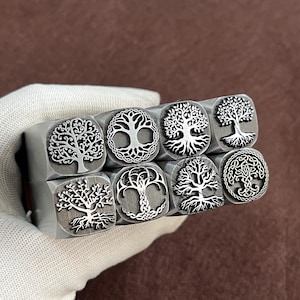 Puede incluir: Ocho sellos metálicos cuadrados, cada uno con un diseño de árbol estilizado diferente. Los diseños de árboles varían en detalle y estilo, algunos incluyen intrincados trabajos de nudos. Los sellos son de metal plateado.