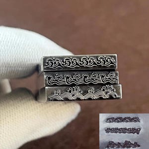 May include: Three rectangular metal stamps with wave pattern designs. The stamps are stacked, showing the intricate details of the wave patterns. The stamps are held by a gloved hand, with a small image of the stamps in the bottom right corner.