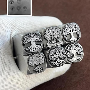 Könnte beinhalten: Nahaufnahme von sechs Metallstempeln mit Lebensbaum-Designs. Jeder Stempel zeigt eine detaillierte Baumillustration, mit Variationen in den Wurzeln, Ästen und im Stil. Die Stempel werden in einem weißen Handschuh gehalten.