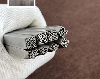 May include: A collection of metal stamps with various decorative patterns. The stamps are held in a white gloved hand. A smaller image in the upper left corner shows the stamped impressions of the designs. The stamps are for crafting or jewelry making.