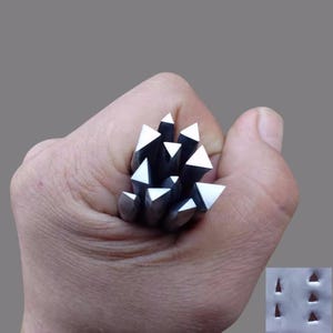 May include: A cluster of silver metal tools with triangular tips, held in a hand. The tools are arranged to resemble a cluster of crystals or spikes. The background is a solid gray.