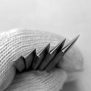 May include: Close-up of five sharp, silver blades arranged in a fan shape, held in a white, textured glove.