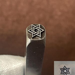 May include: A close-up of a metal stamp with a six-pointed star design. The star is made of two overlapping triangles, creating a complex geometric pattern.