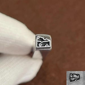 Peut inclure: Un tampon en métal avec un motif de part de fromage. Le tampon est carré avec un contour détaillé de la forme du fromage et des trous intérieurs. L'image est sur un fond marron.