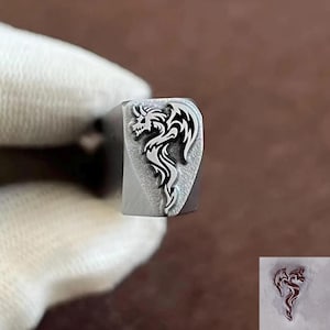 May include: A metal stamp with a dragon design. The dragon is depicted in black and white, with intricate details. The stamp is rectangular with a curved top. A smaller, red version of the dragon is in the corner.
