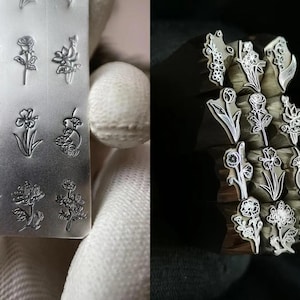 Pu&ograve; includere: Un set di 12 timbri per fiori in metallo per l'artigianato. I timbri sono disposti in due file di sei, con ogni timbro che presenta un diverso design floreale. I timbri sono realizzati in metallo e hanno una finitura lucida.