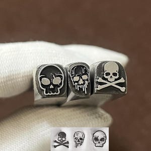 Puede incluir: Tres sellos de metal con diseños de calaveras. El primer sello muestra una calavera estilizada, el segundo una calavera con efecto de goteo y el tercero una calavera con huesos cruzados. Debajo se muestra una impresión de cada sello.