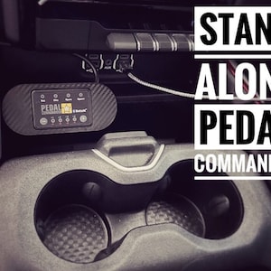 Op de afbeelding: Een zwart Pedal Commander-apparaat met een sterlogo en de tekst "Pedal Commander" en "Bluetooth" op het display. Het apparaat is geïnstalleerd in de middenconsole van een auto, met de tekst "STAND ALONE PEDAL COMMANDER" zichtbaar op de achtergrond.