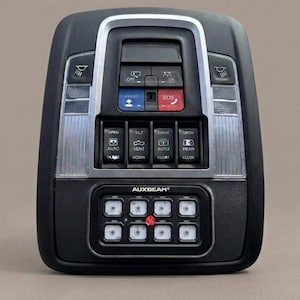 Puede incluir: Panel de control automotriz negro con molduras plateadas, con varios botones e indicadores luminosos. Incluye botones etiquetados como "ASSIST", "SOS", "OPEN", "CLOSE" y la marca "AUXBEAM". El panel tiene forma rectangular con bordes redondeados.
