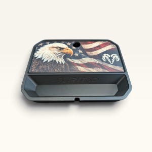 Op de afbeelding: Een zwarte kunststof bak met een bedrukte afbeelding van een Amerikaanse zeearend, een Amerikaanse vlag en een ram-logo. De bak heeft een opbergvak met de in reliëf aangebrachte tekst FLIPIT3D op de achterwand van de binnenzijde.