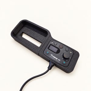 May include: A black HIKE IT high performance controller mounted in a textured black plastic housing. The device features a digital display, a circular control knob, several buttons with directional arrows, and a black power cable extending from the base.