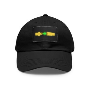 May include: A black baseball cap with a yellow and green graphic of a seatbelt buckle. The graphic is on a black patch sewn onto the front of the cap.