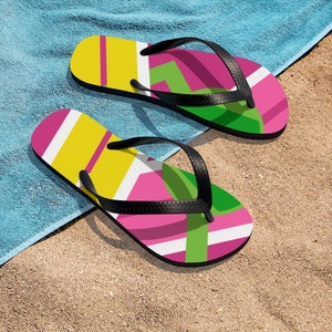 May include: A pair of colorful flip-flops with a geometric pattern in pink, yellow, green, and white. The flip-flops have black straps.