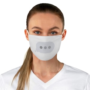 May include: White face mask featuring a gray speech bubble with three gray dots. The mask has white ear loops and covers the nose and mouth. The person is wearing a white v-neck shirt.