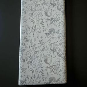 May include: A rectangular package wrapped in white paper with a gray floral and fairy pattern. The word "Light" is printed in black at the bottom. The design includes fairies, flowers, and the letters "L" and "H".