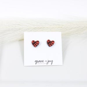 Peut inclure: Une paire de boucles d'oreilles &agrave; clous en forme de c&oelig;ur avec un motif de ballon de basket orange textur&eacute; et des lignes noires. Les boucles d'oreilles sont fix&eacute;es sur une carte de pr&eacute;sentation blanche avec le texte grace + joy collective.