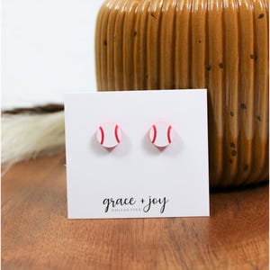 May include: A pair of white and red baseball stud earrings. The earrings are on a white card with the text "grace + joy collective".