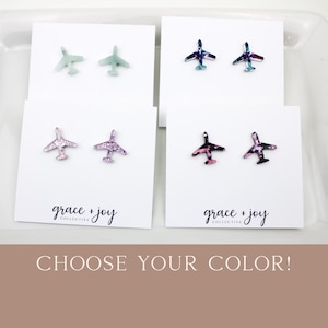May include: Airplane stud earrings in four color options: mint green, iridescent blue-purple, glittery pink-purple, and black-pink. Each pair is displayed on a white card with the "grace + joy collective" logo. The text "CHOOSE YOUR COLOR!" is at the bottom.
