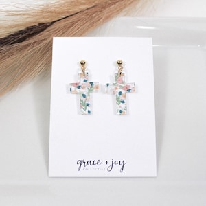 May include: A pair of gold cross earrings with a floral pattern. The earrings are on a white card with the text "grace + joy collective".