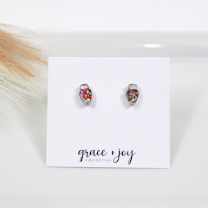 Könnte beinhalten: Ein Paar kleine, farbenfrohe, glitzernde Glühbirnen-Ohrringe. Die Ohrringe befinden sich auf einer weißen Karte mit dem Text "grace + joy collective".
