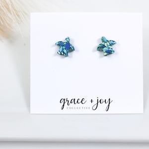Könnte beinhalten: Ein Paar blaue und grüne Schildkröten-Ohrstecker auf einer weißen Karte mit dem Text "grace + joy collective".