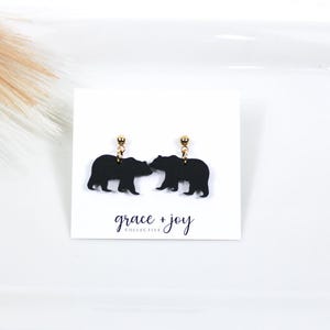 May include: Black bear silhouette earrings with gold posts. The earrings are on a white card with the text "grace + joy collective".