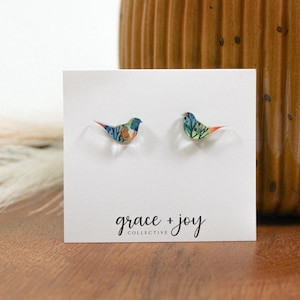 Peut inclure: Une paire de petites boucles d'oreilles en forme d'oiseau color&eacute; sur une carte blanche avec le texte "grace + joy collective".