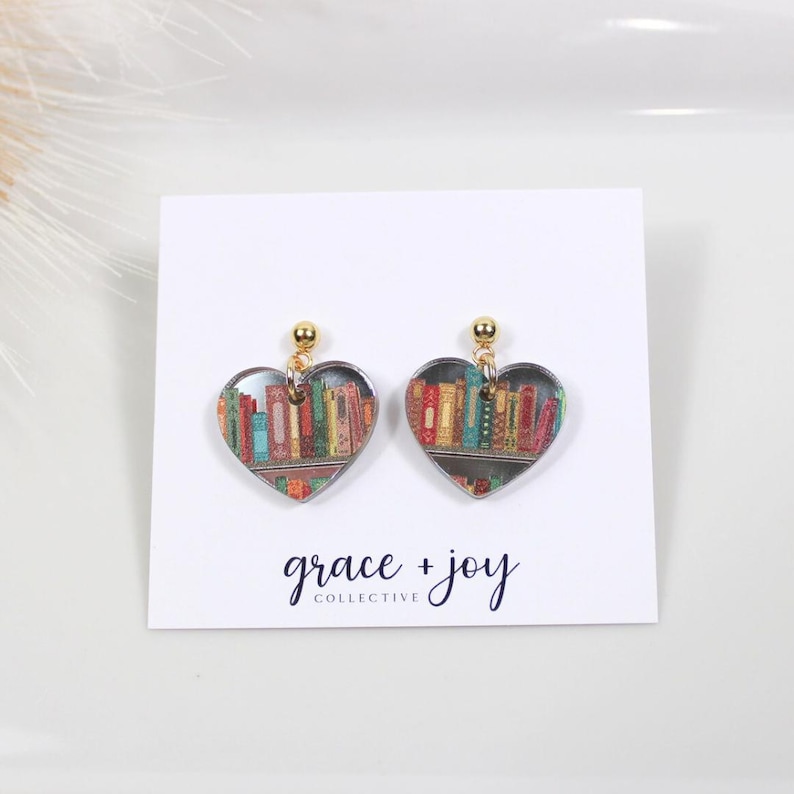 Peut inclure: Une paire de boucles d'oreilles en forme de c&oelig;ur avec une finition dor&eacute;e. Les boucles d'oreilles pr&eacute;sentent un design clair et transparent avec une image color&eacute;e d'une biblioth&egrave;que remplie de livres &agrave; l'int&eacute;rieur de chaque c&oelig;ur.