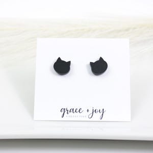 Op de afbeelding: Een paar zwarte katvormige oorstekers op een witte kaart. De kaart heeft de tekst "grace + joy COLLECTIVE" in cursief. De oorbellen worden getoond op een wit oppervlak.