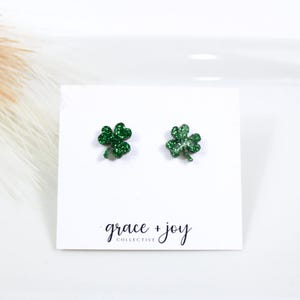 May include: A pair of green glitter shamrock stud earrings on a white card with the text "grace + joy collective".