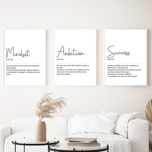 Puede incluir: Tres impresiones enmarcadas blancas con texto negro sobre fondo blanco. Las impresiones se titulan "Mindset", "Ambition" y "Success". Cada impresión incluye una definición de la palabra. Las impresiones están colgadas en una pared blanca sobre un sofá blanco y dos mesas de café negras y blancas.