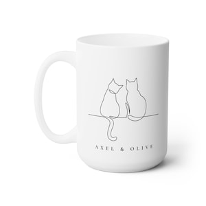 May include: White ceramic mug with a black line drawing of two cats sitting back to back. The text "AXEL & OLIVE" is printed below the cats.