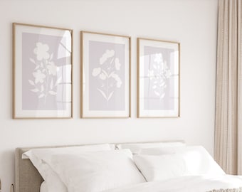 May include: A white bed with a beige knitted throw blanket and white pillows. Three framed prints with floral designs hang on the wall above the bed.