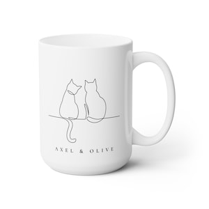 Pu&ograve; includere: Tazza in ceramica bianca con un disegno a linea nera di due gatti seduti uno di fronte all'altro. Il testo "AXEL & OLIVE" &egrave; stampato sotto i gatti.