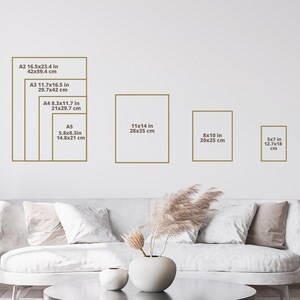 May include: A white couch with pillows in a living room with a white wall. The wall has a chart showing different sizes of paper prints in inches and centimeters. The sizes include 16.5x23.4 inches, 11.7x16.5 inches, 8.3x11.7 inches, 5.8x8.3 inches, 11x14 inches, 8x10 inches, and 5x7 inches.