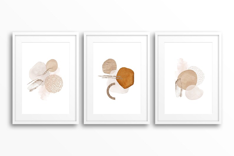 Op de afbeelding: Drie ingelijste prints met abstracte vormen in tinten bruin en beige. De vormen zijn organisch en lijken op cirkels, ovalen en lijnen.