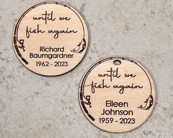 May include: Two round wooden memorial ornaments with the phrase "until we fish again" and a fishing rod design. One ornament is inscribed with "Richard Baumgardner 1962-2023" and the other with "Eileen Johnson 1959-2023".