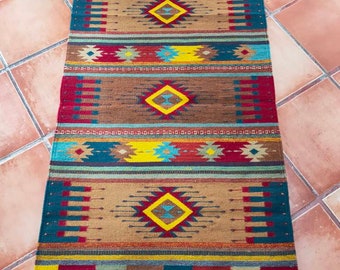 May include: A colorful southwestern style rug with geometric patterns in shades of red, blue, yellow, and brown. The rug has a fringe border.