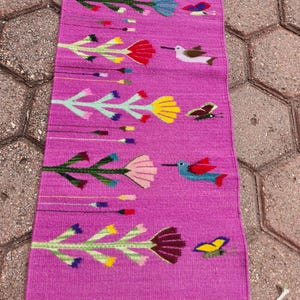 Peut inclure: Un tapis de couloir magenta tissé à la main, orné d'un motif répété de fleurs et d'oiseaux stylisés de différentes couleurs. Le tapis a une bordure frangée et est probablement fait de fibres naturelles. Sa longueur est d'environ 150 cm.