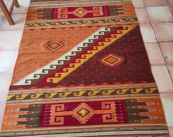 May include: A brown, red and yellow patterned rug with a geometric design. The rug has a fringed border.