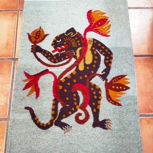 Puede incluir: Una alfombra gris y blanca con un diseño de jaguar marrón y naranja. El jaguar está rodeado de flores estilizadas.