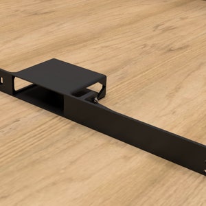 Puede incluir: Soporte de estante de metal negro con una abertura rectangular. El soporte tiene varios agujeros para montaje.
