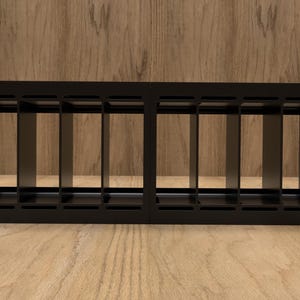 May include: A black rack mount enclosure with multiple vertical compartments. The enclosure is made of metal and has mounting holes on the sides. The background is a light brown wooden surface.