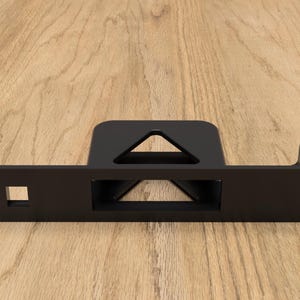 May include: A black metal bracket with a rectangular base and a raised section featuring a triangular cutout. The bracket has a square hole and three smaller holes on one end, and an L-shaped extension on the other.