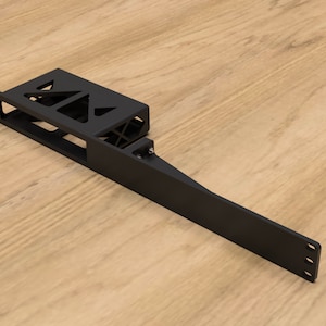 Puede incluir: Soporte de metal negro con una abertura rectangular y un brazo largo y delgado que se extiende desde el lado. El soporte tiene una serie de pequeños agujeros a lo largo del borde del brazo.