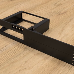 Puede incluir: Un componente de montaje en rack de metal negro con un marco rectangular y un brazo extendido. El componente tiene múltiples ranuras de ventilación y orificios de montaje. El artículo está diseñado para equipos electrónicos y se muestra sobre una superficie de madera.