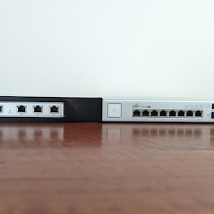 Könnte beinhalten: Ein silberner UniFi 8-Port Gigabit-Ethernet-Switch mit einem schwarzen Netzteil und einem schwarzen UniFi 5-Port Gigabit-Ethernet-Switch.
