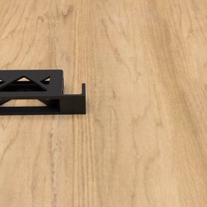 Könnte beinhalten: Drei schwarze Metallwinkel zum Befestigen eines Regals oder eines anderen Objekts. Die Winkel sind aus robustem Metall gefertigt und haben ein schlichtes, modernes Design.