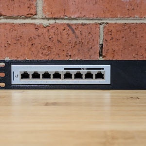 Könnte beinhalten: Eine schwarze Metall-Wandplatte mit acht Ethernet-Ports, die von 1 bis 8 nummeriert sind. Die Platte hat eine silberne Frontplatte mit dem aufgedruckten Text "POE OUT".