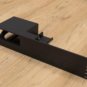 May include: Black metal rack with a rectangular opening and a long, narrow extension. The rack has multiple holes along the side.